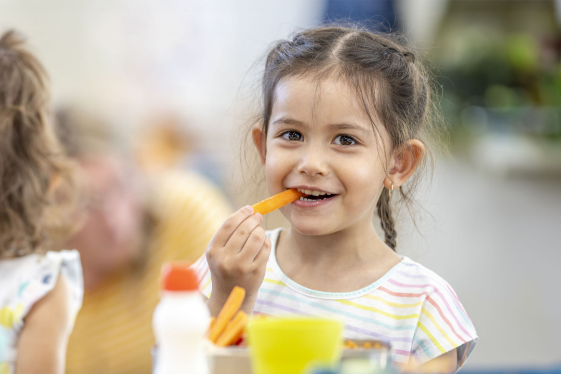 girl smiling while eating a carrot