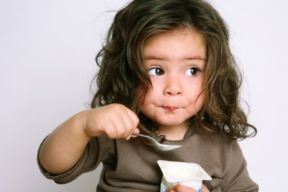 girl with brwon sweatshirt eating yugort with a spoon